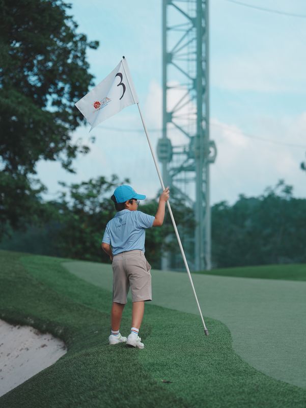 Junior golfer holding the flag on a green at HKGTA, Sai Kung